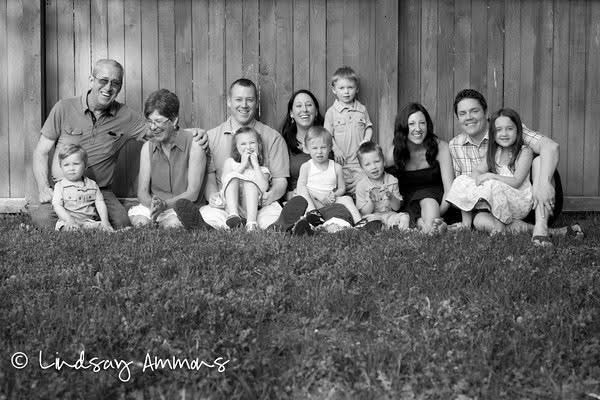 Three generations sitting together on the grass — grandparents, parents, and grandchildren — laughing in the afternoon light.
