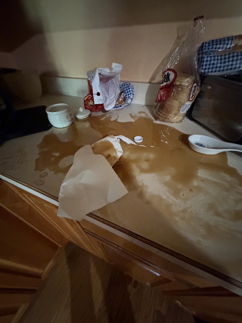Thick amber syrup pooled across a kitchen counter, a paper towel barely covering the mess.